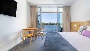 Une chambre d’hôtel moderne dotée d’un grand lit, d’un bureau avec des chaises, d’une télévision à écran plat et offrant une vue sur l’eau.