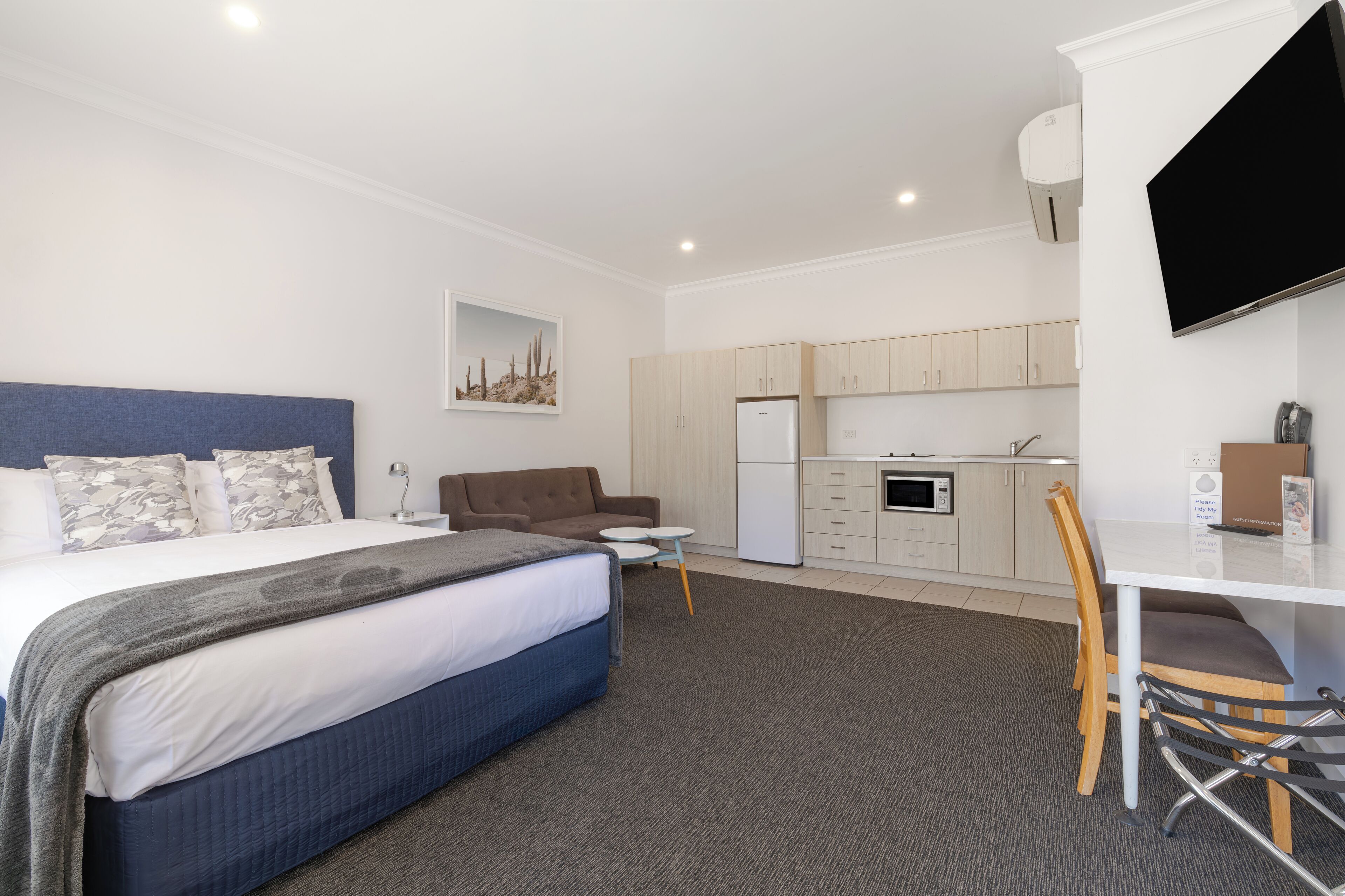 A hotel room with a bed, a desk, a chair, a kitchenette, and a TV.