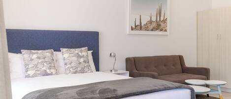A bedroom with a large bed, a brown sofa, a small round table, and a framed picture on the wall.