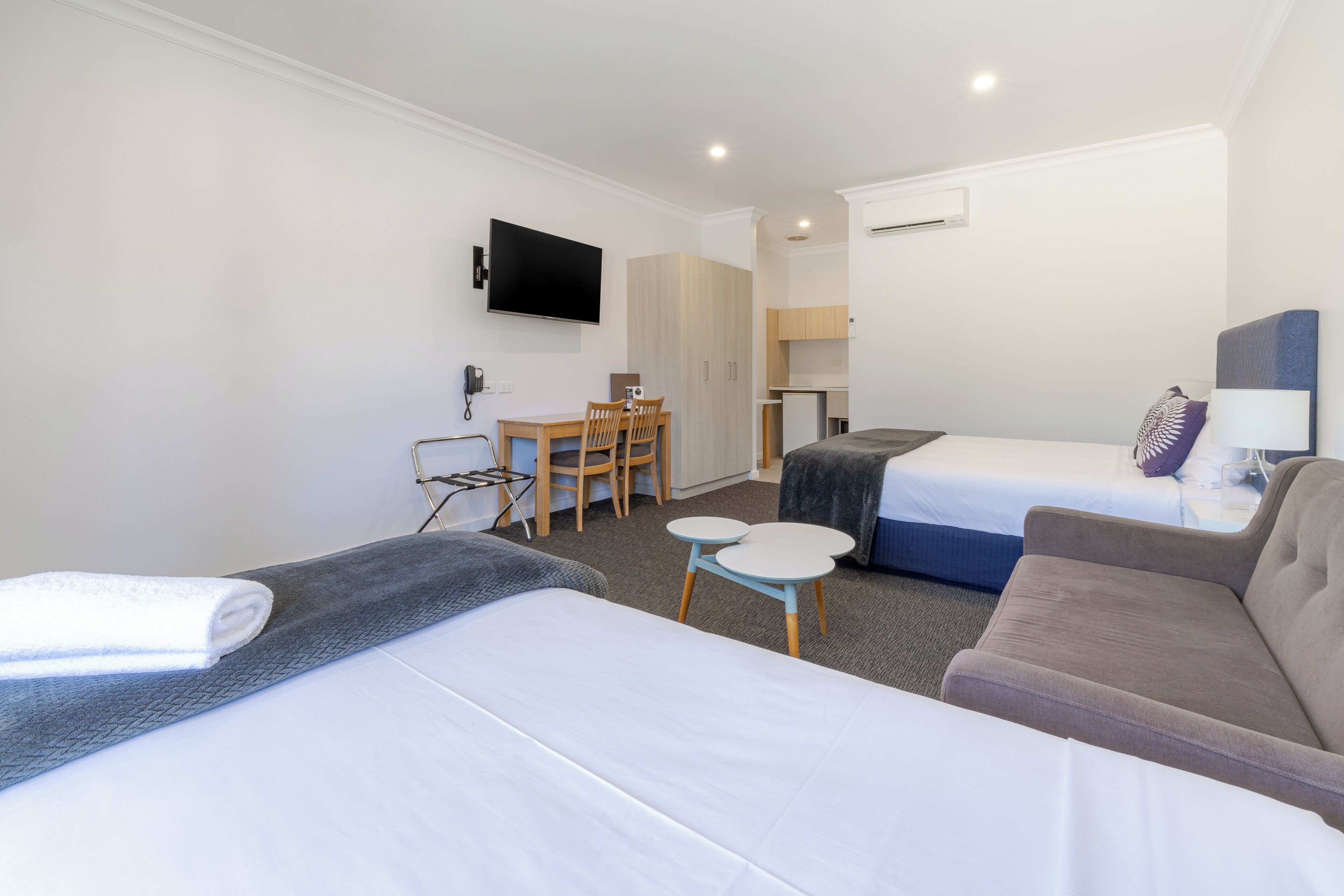 Une chambre d’hôtel avec deux lits, un bureau, une chaise, une télévision et une petite kitchenette.