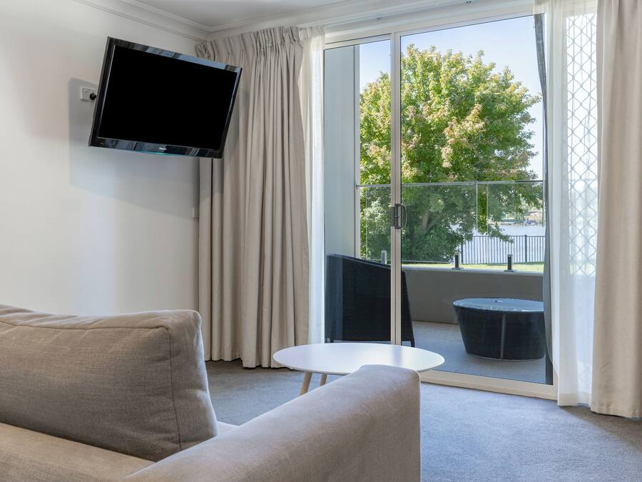 A modern living room with a sofa, a flat-screen TV mounted on the wall, and a balcony with a table and chairs.