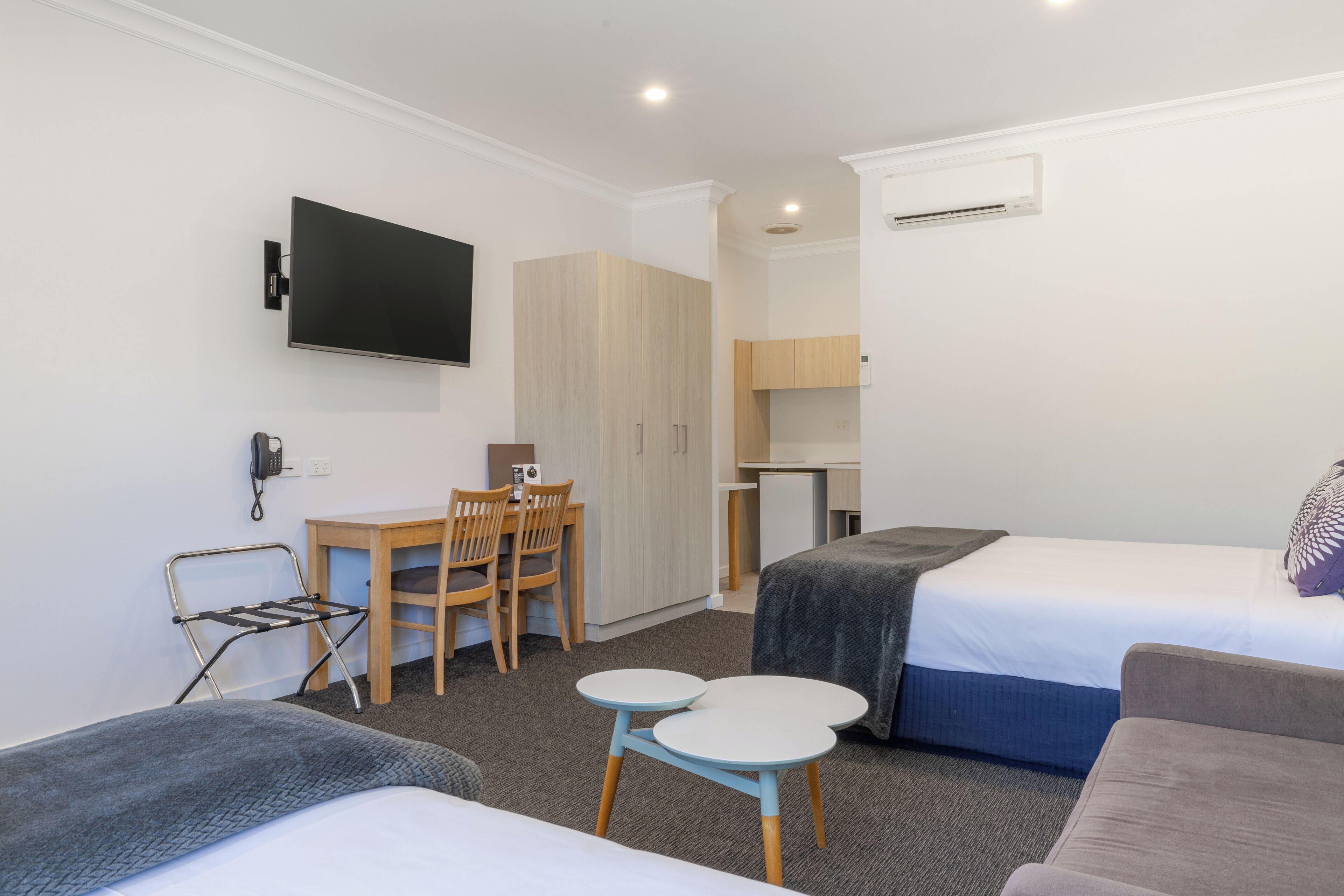 A hotel room with a bed, a desk, a chair, a small table, and a TV.