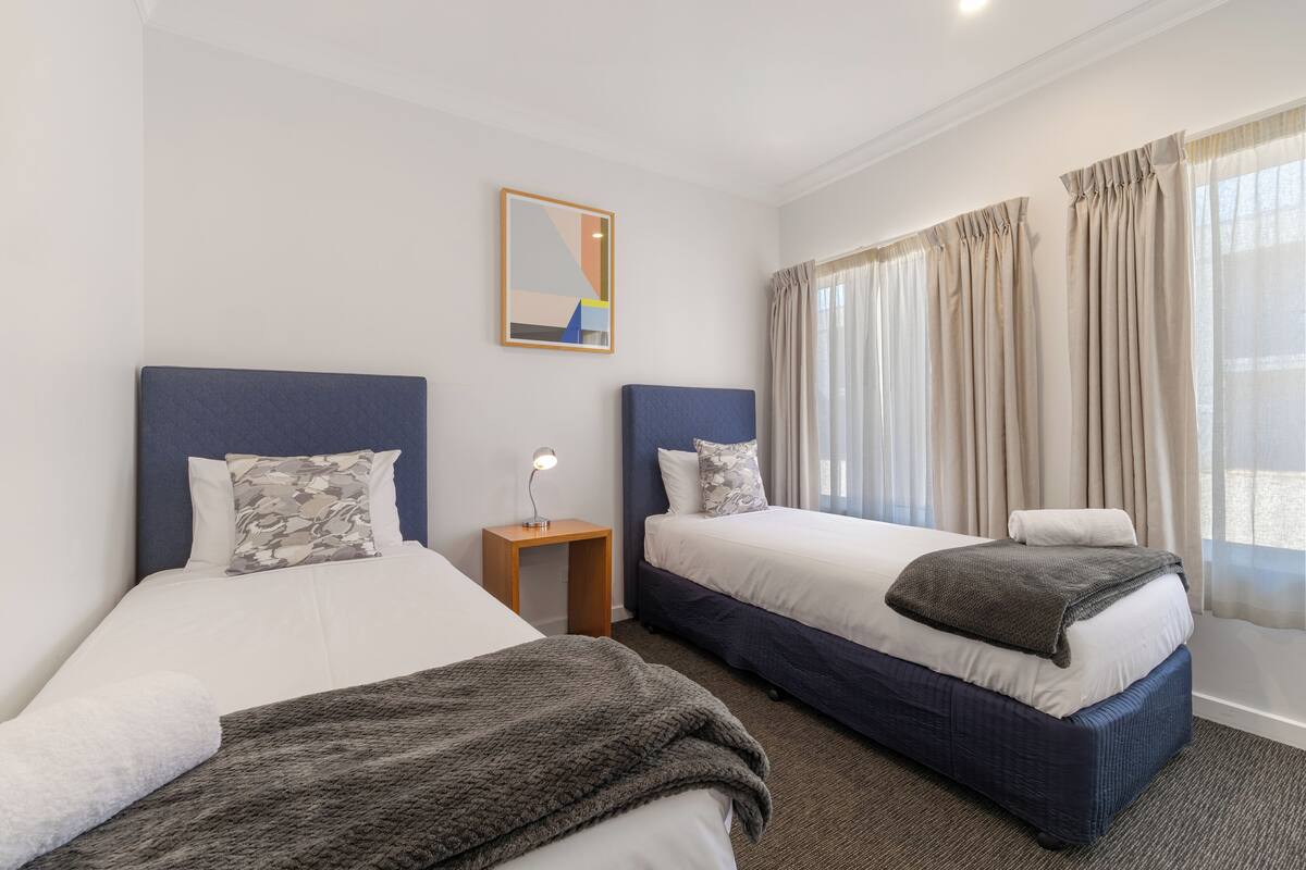 Habitación de hotel con dos camas, una mesita de noche, una lámpara y un cuadro en la pared.