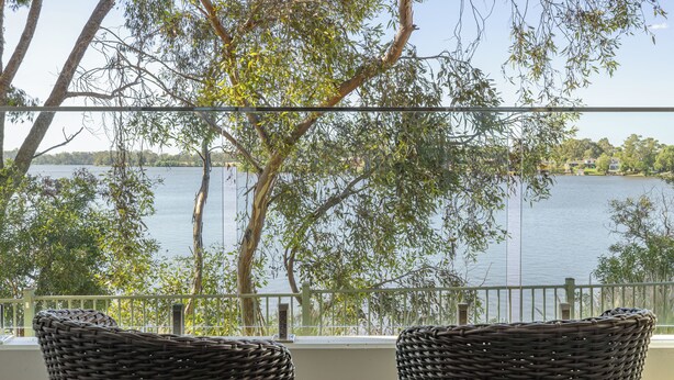 Un balcon avec des fauteuils en osier donnant sur un lac, entouré d’arbres.