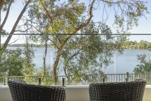 A balcony with wicker chairs overlooking a lake, surrounded by trees. - Nagambie Waterfront Motel  (Nagambie)
