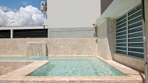 Ein Pool auf dem Dach mit klarem Wasser, Steinwänden und Blick auf Himmel und Wolken.