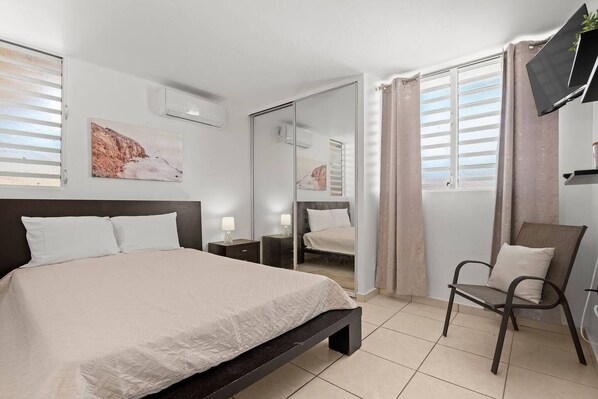 Un dormitorio moderno con una cama grande, una silla, un televisor y un espejo.