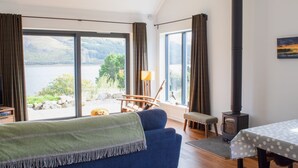 A cozy room with a large window, a sofa, a table, and a fireplace. - Tigh Na Allt by Interhome (Mid Skye)