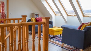 A loft-style room with a wooden staircase, a blue sofa, a yellow ottoman, and a colorful rug. - Vacation home Solace by Interhome (North Skye)
