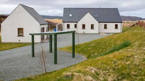 A row of white buildings with grey roofs, a gravel path, and a grassy hill in the background. - Vacation home Solace by Interhome (North Skye)