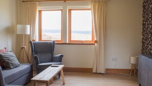 A living room with a sofa, armchair, wooden coffee table, and two windows with curtains. - Vacation home Solace by Interhome (North Skye)