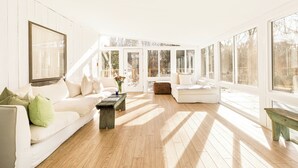 Un salón luminoso e inundado de sol, con un sofá blanco, una mesita de centro y un banco.