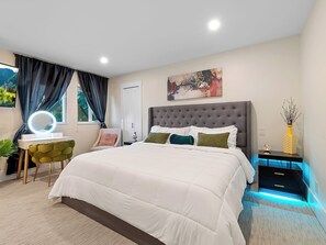 A modern bedroom with a large bed, a vanity with a mirror, a chair, and a nightstand with a lamp. - Private Luxury Resort steps in Langley Event Centre- w/ hot tub, basketball (Langley Township)