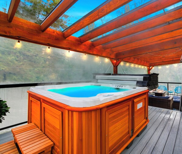 A hot tub under a wooden pergola with string lights, surrounded by wooden deck and outdoor furniture. - Private Luxury Resort steps in Langley Event Centre- w/ hot tub, basketball (Langley Township)