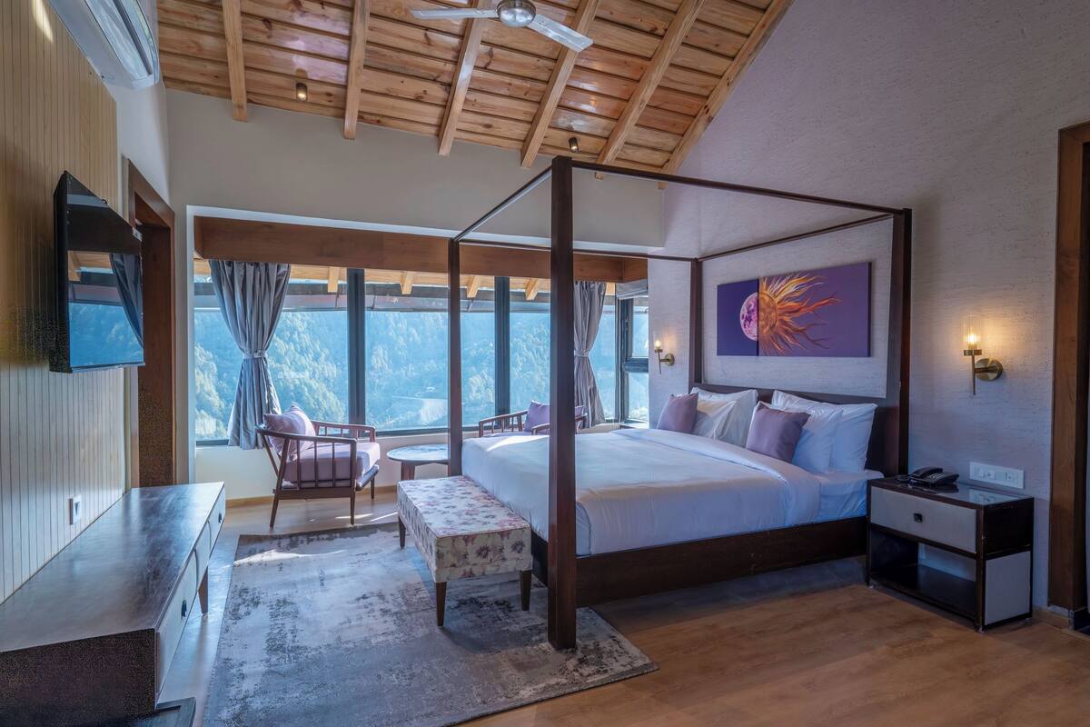 A four-poster bed with a view of mountains, a flat-screen TV, a bedside table, and a nightstand.