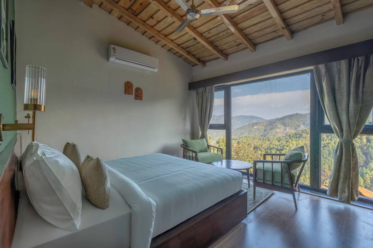 A bedroom with a bed, a chair, a table, and a view of the mountains.