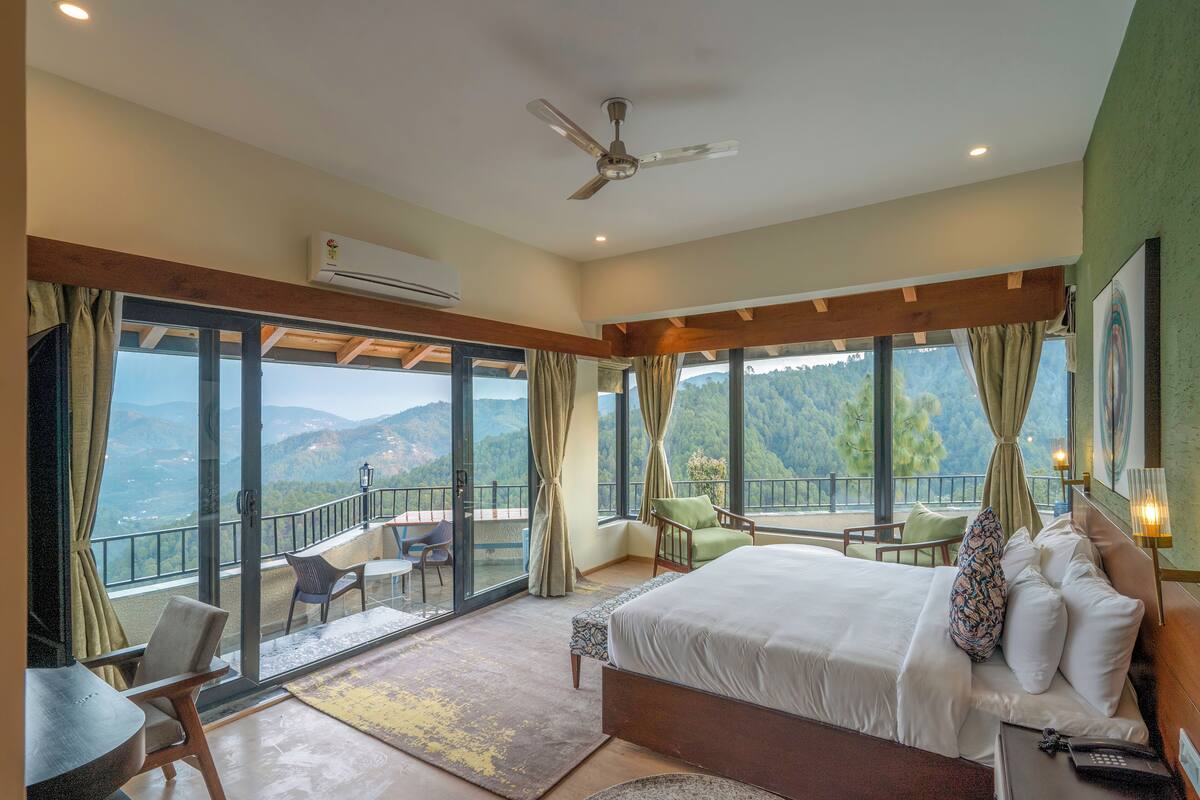 A spacious bedroom with a large bed, a balcony with a view of the mountains, and a ceiling fan.