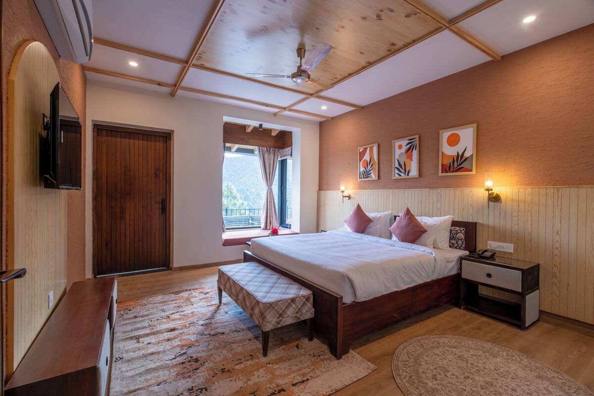 A bedroom with a wooden bed, bedside tables, a bench, a large window with curtains, and artwork on the wall.