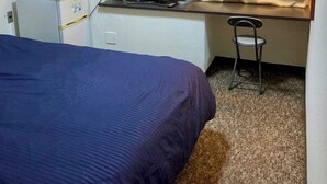 Una habitación de hotel pequeña con una cama individual, un escritorio con una computadora portátil, una silla y una ventana con cortinas.