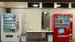 Una habitación con dos máquinas expendedoras, una mesa y un cubo de basura.