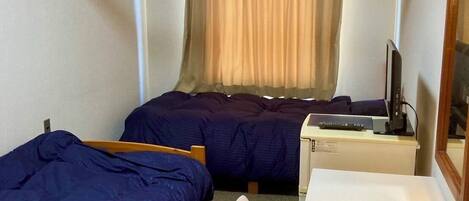 Una habitación de hotel pequeña con dos camas individuales, un escritorio con computadora y una ventana con cortinas.