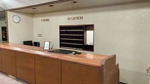 Un mostrador de recepción con un reloj, una caja registradora y un tablón de anuncios.