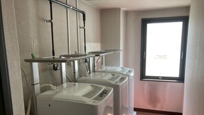 Un área de lavandería con tres lavadoras apiladas, un estante metálico arriba y una ventana con vistas.