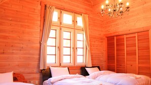 Una habitació de fusta amb dos llits, una finestra amb cortines, un penjador de cristall i un armari.