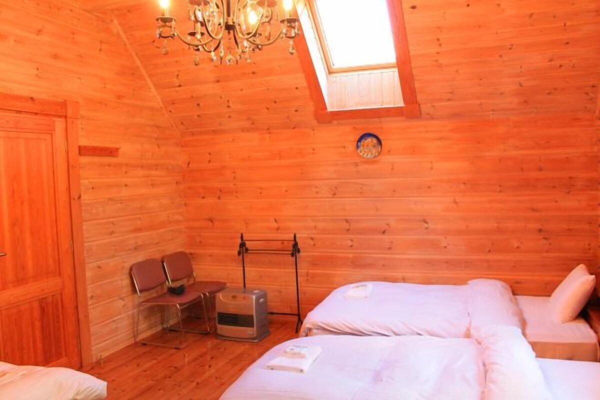 Een houten kamer met twee bedden, een kroonluchter, een tafeltje en een raam.