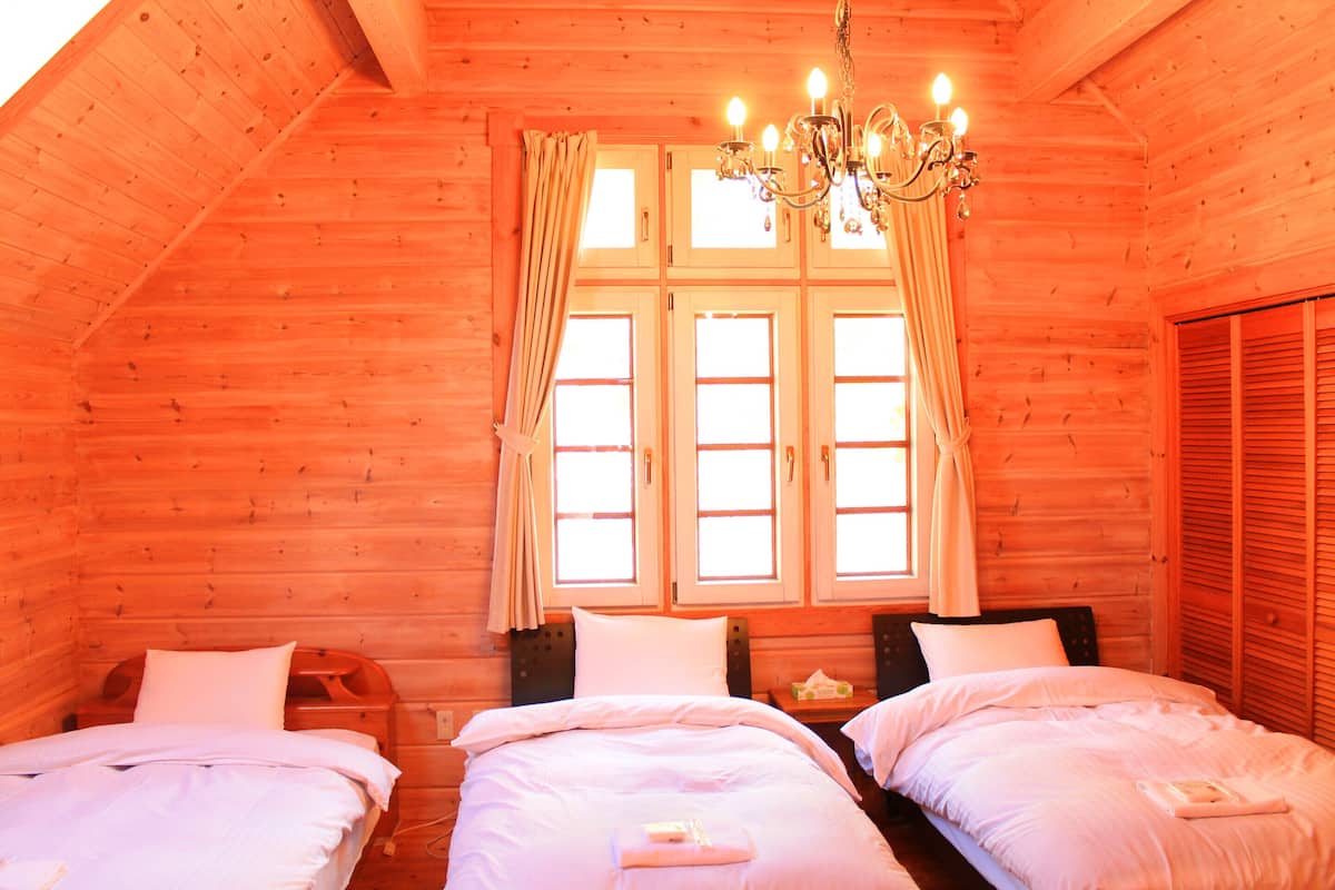 Un dormitorio de cabaña de madera acogedor, con dos camas, una araña y un gran ventanal con cortinas.