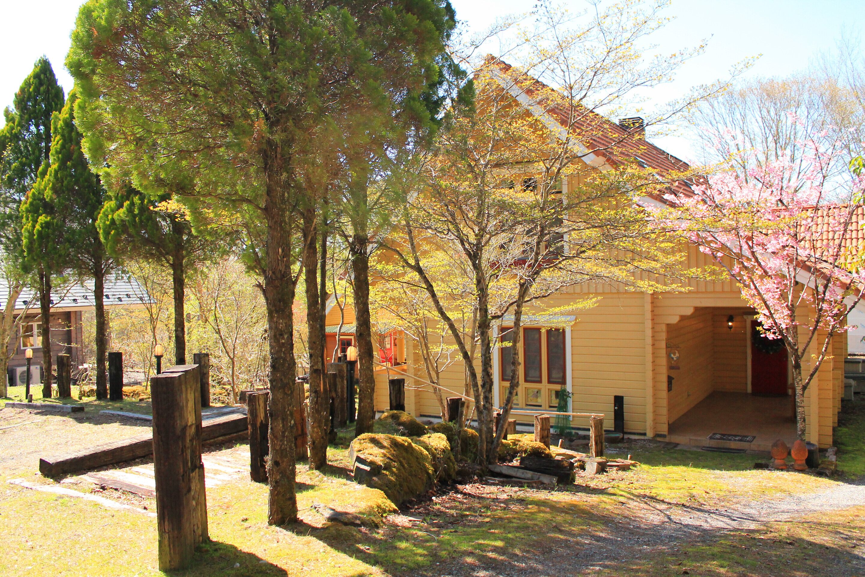 A yellow building with a red roof, surrounded by trees and a wooden fence.