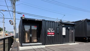 Ein schwarzes, containerartiges Gebäude mit einem Schild, das "The Yard" und "Rezeption" als Hotelkomplex ausweist.