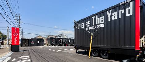 Un conteneur noir sur lequel on peut lire « HOTEL R9 The Yard » et « HOTEL GROUP », garé dans une rue sous un ciel dégagé.