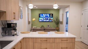 A modern kitchen with a large island, wooden cabinets, and a flat-screen TV mounted on the wall.