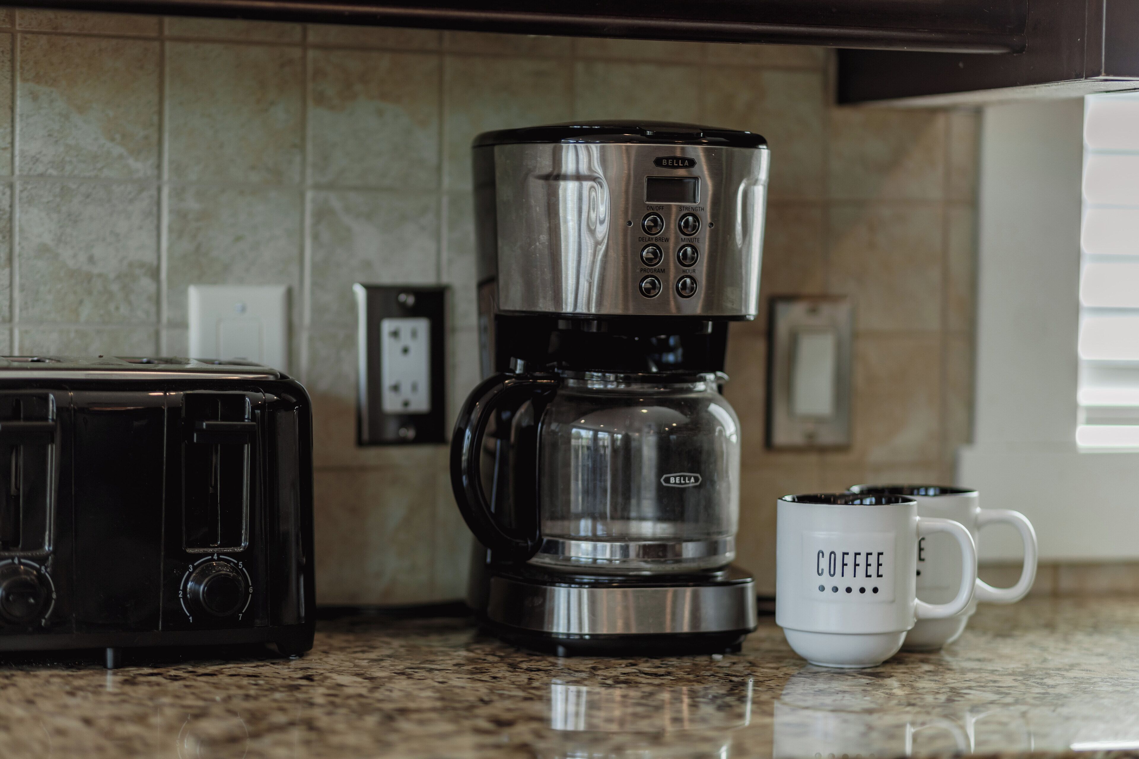 Una cocina con cafetera, tostadora y dos tazas de café sobre la encimera.