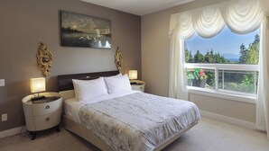 A bedroom with a large bed, two bedside tables with lamps, a painting on the wall, and a window with curtains. - Luxury Rainbow House, Private with Pool Table, and Oceanview (Nanaimo)