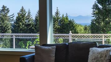 Habitación con vistas a un balcón, un sofá y una ventana que da a un bosque y montañas.