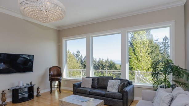A spacious living room with a large flat-screen TV, leather sofas, a coffee table, and a chandelier. - Luxury Rainbow House, Private with Pool Table, and Oceanview (Nanaimo)