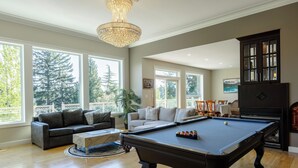 A spacious living room with a pool table, a dark wooden cabinet, and a chandelier. - Luxury Rainbow House, Private with Pool Table, and Oceanview (Nanaimo)