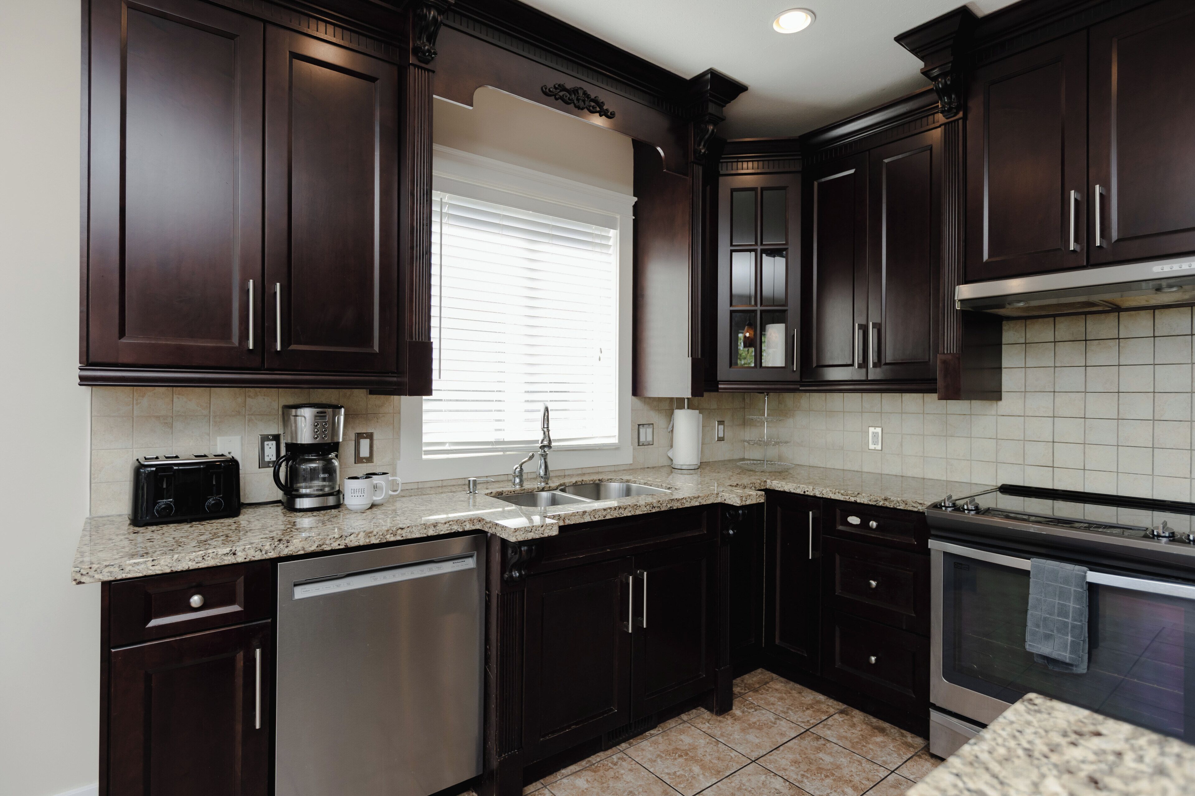A kitchen with dark wood cabinets, a stainless steel dishwasher, a built-in oven, and a granite countertop.