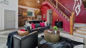A spacious living room with a black leather sofa, a round coffee table, and a staircase leading to a red upper level. - Luxury Romantic Cabin - KingBed ~ Strip Lounge (Broken Bow)