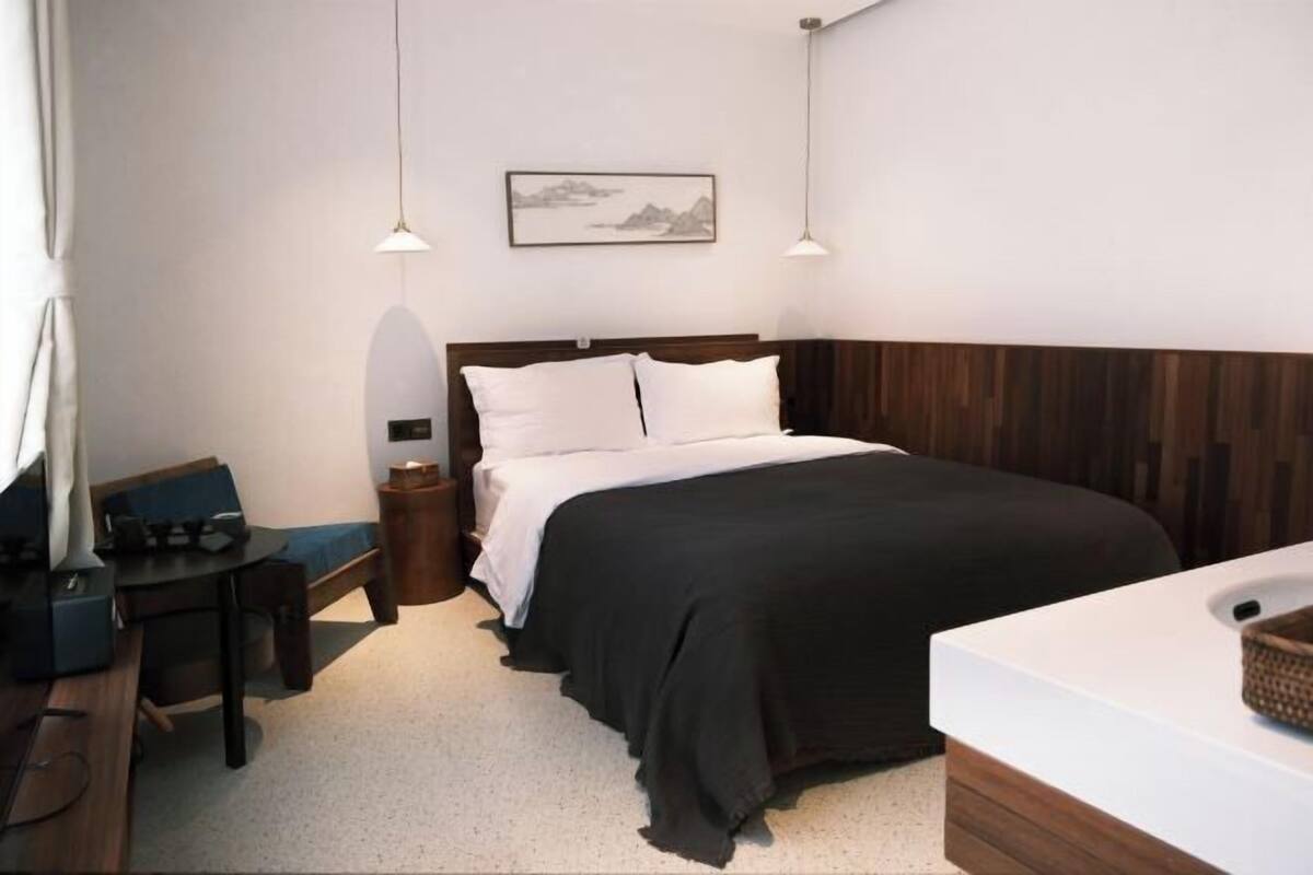 A bedroom with a bed, bedside table, chair, and a desk with a lamp.