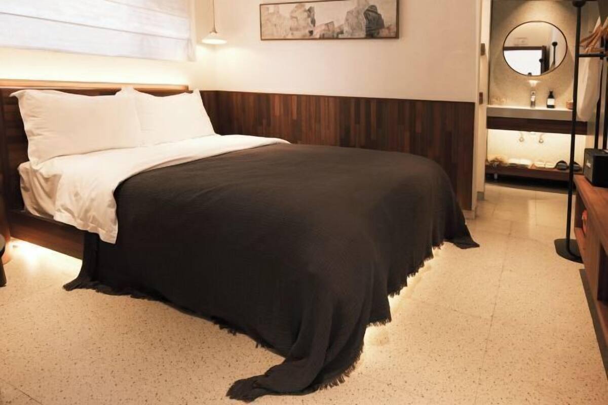 A bedroom with a bed, a nightstand, a mirror, and a wall-mounted artwork.