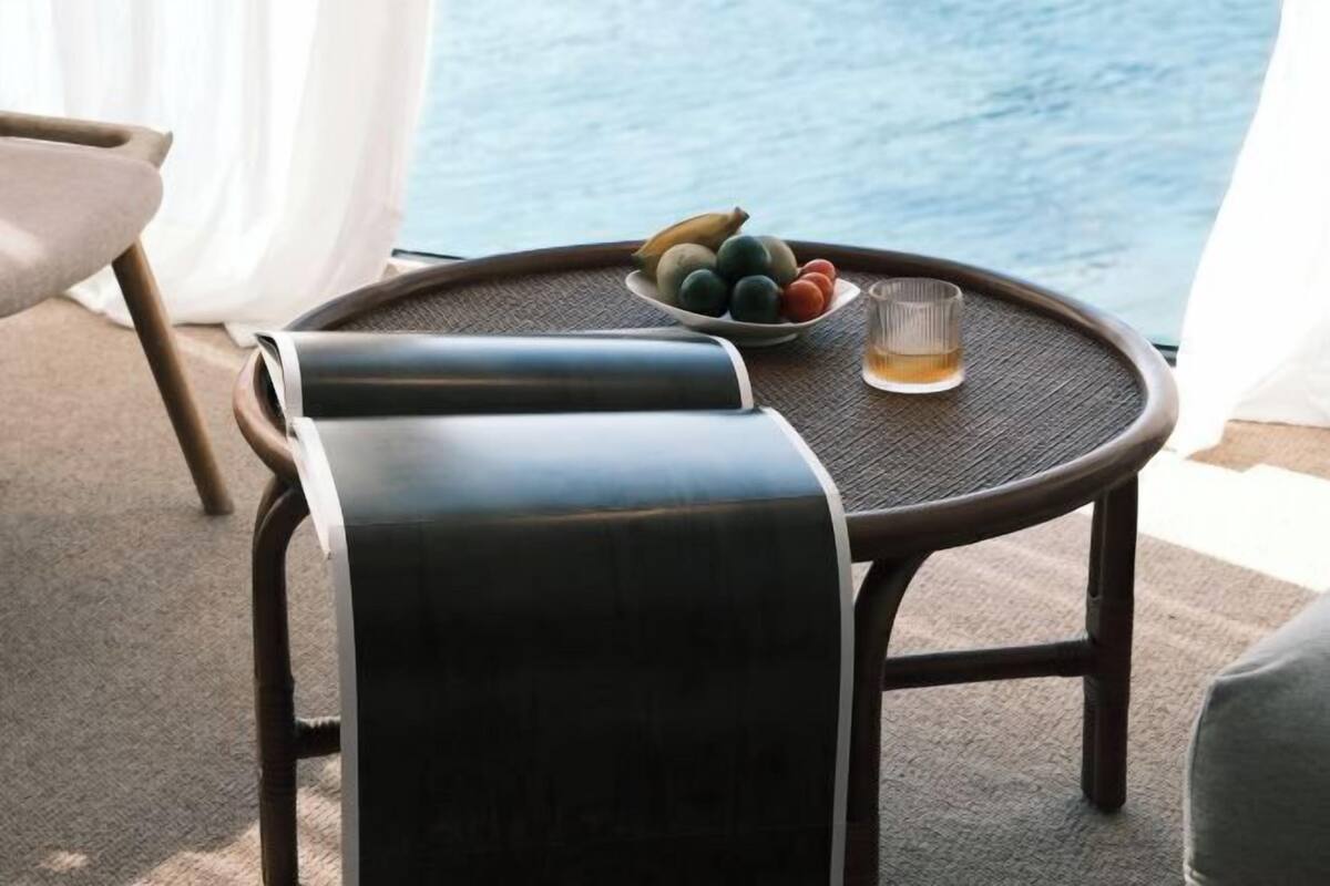 A round table with a woven surface, a bowl of fruit, and a glass of beverage.