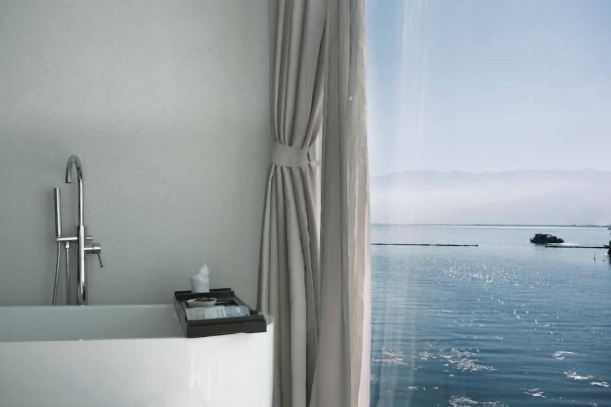 A bathroom with a bathtub, a shower, and a window with a view of the sea.