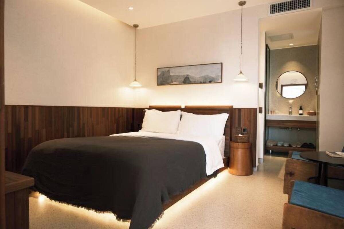 A hotel room with a bed, bedside table, lamp, and a view of the bathroom.