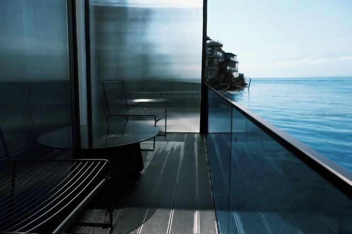 A balcony with a glass railing overlooking the sea, a table, and two chairs.