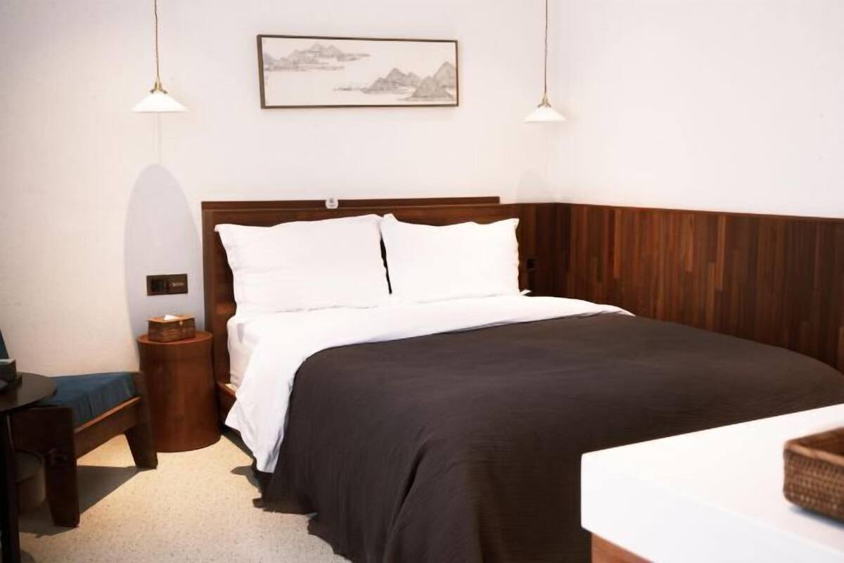 A neatly arranged bedroom with a wooden headboard, a bed with white bedding, a bedside table, and a lamp.