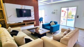 Un soggiorno moderno con una TV a schermo piatto montata su una parete in marmo, un divano blu, un divano beige e un tavolino da caffè.