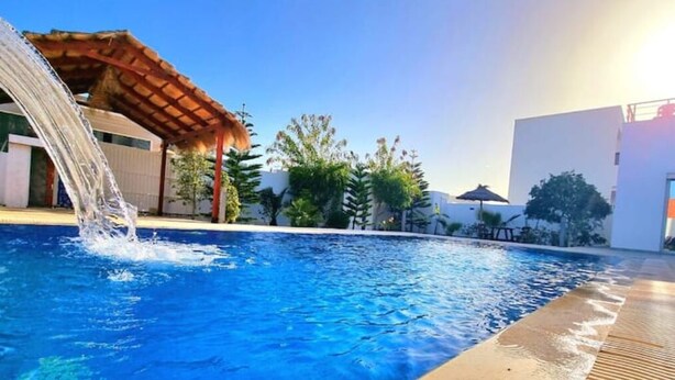 Una piscina con cascata, circondata da edifici moderni e vegetazione.